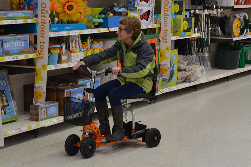 Person navigating a superstore aisle on a compact orange SupaScoota mobility scooter.