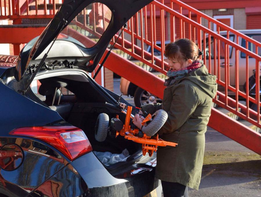 A woman stowing a folded SupaScoota mobility scooter into her car boot for transport.