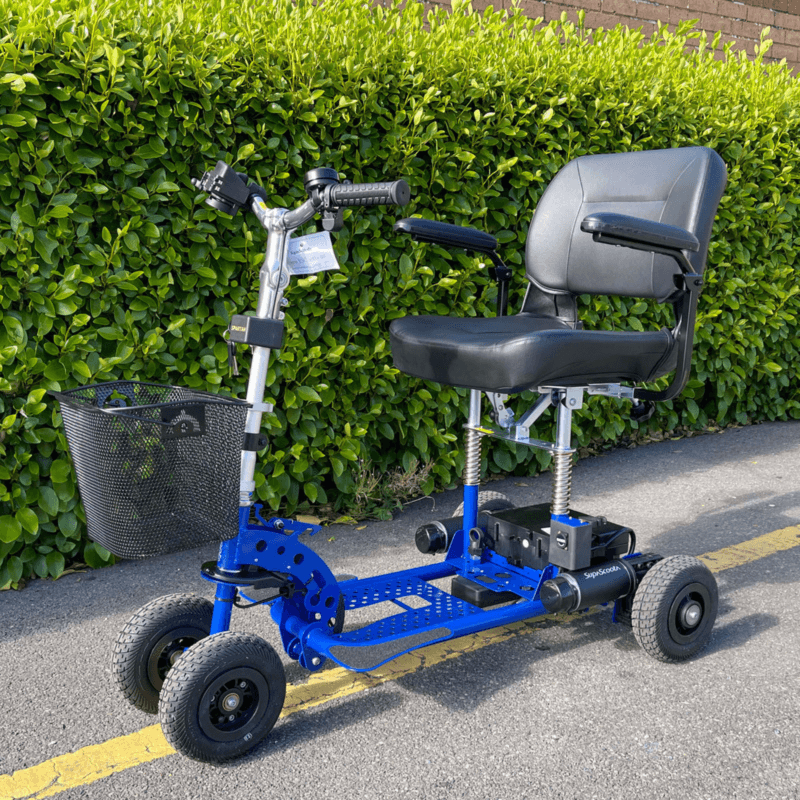 SupaScoota Spartan mobility scooter with basket, parked outdoors by a lush hedge in sunlight.