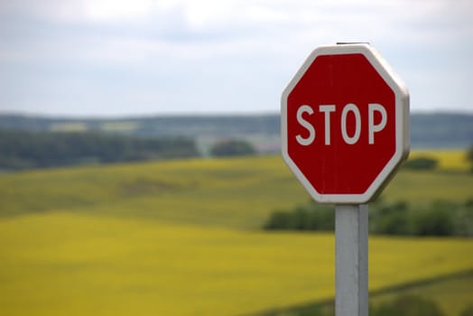 Stop sign on a post with a green and yellow field in the background.