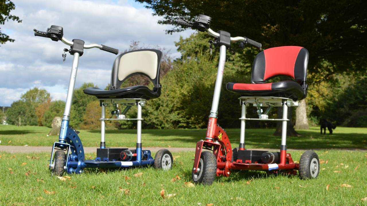 Two SupaScoota's parked on the grass in a park, on a sunny day.